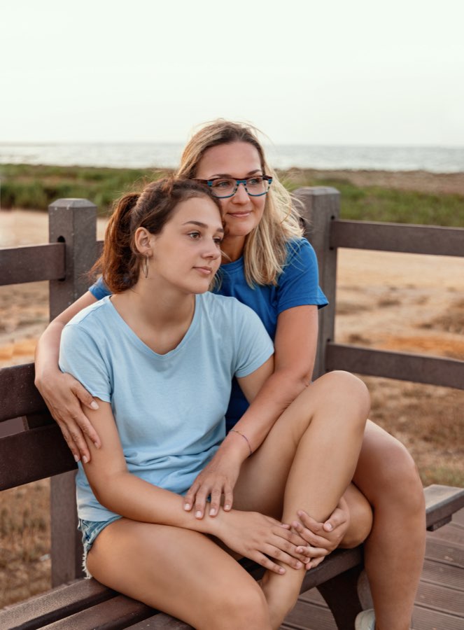 A mother and teenage daughter sitting together at the coast